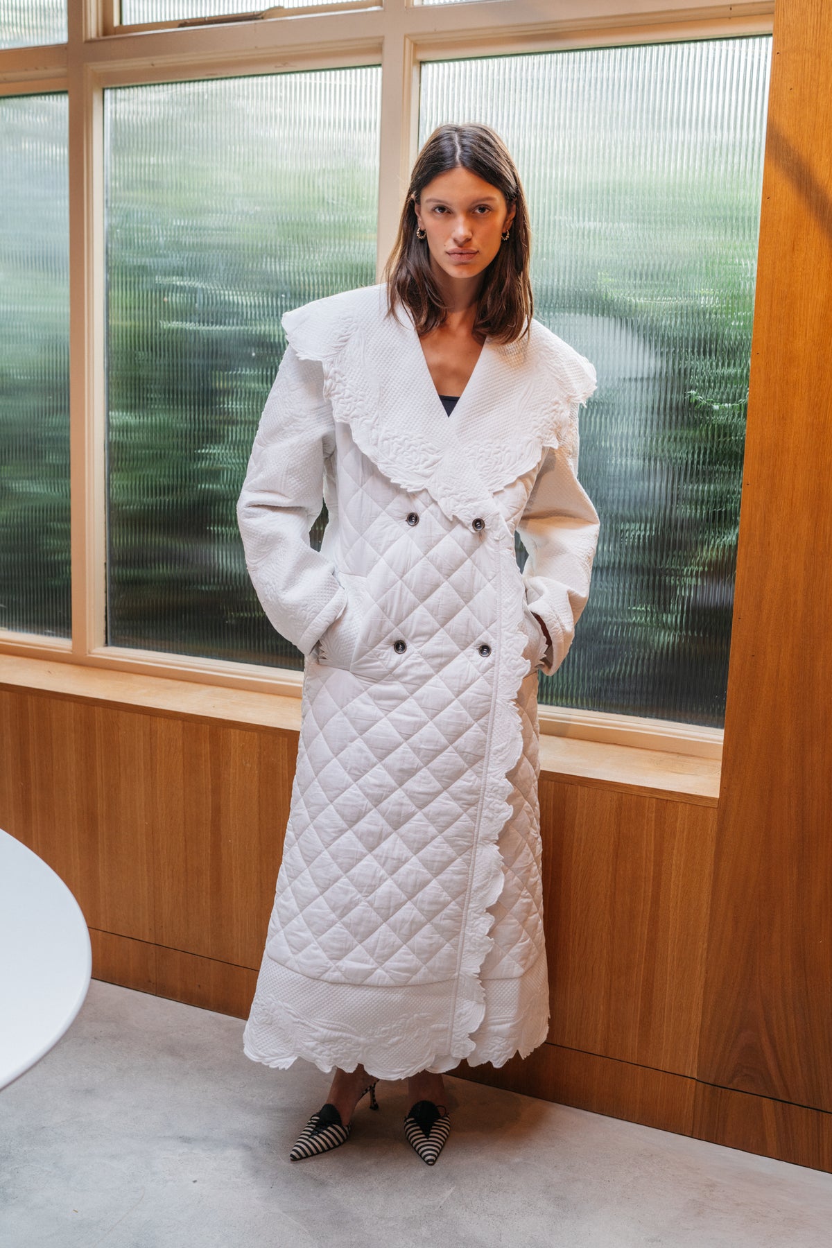 Girl standing in front of frosted windows, wearing an ivory quilted trench coat.