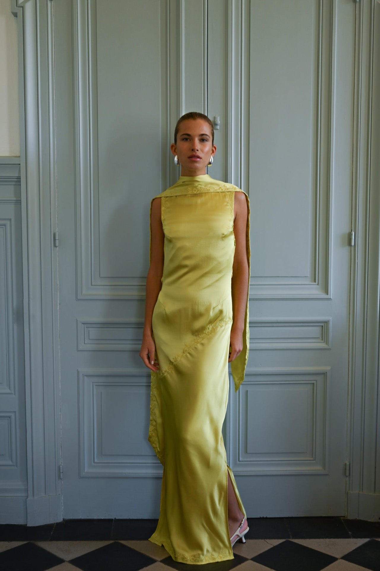 Woman in a chartreuse dress standing against a paneled wall.